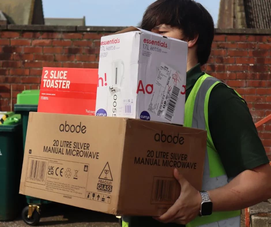 A SHAX team member carrying a kettle, toaster, and microwave for a household